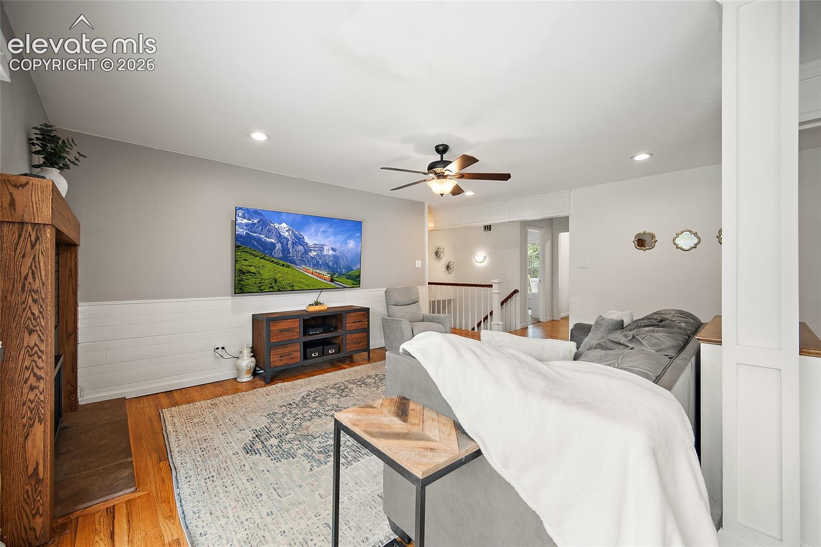 Wood-finish flooring, half-wall wood paneling, wood-framed fireplace mantel, and recessed ceiling lighting