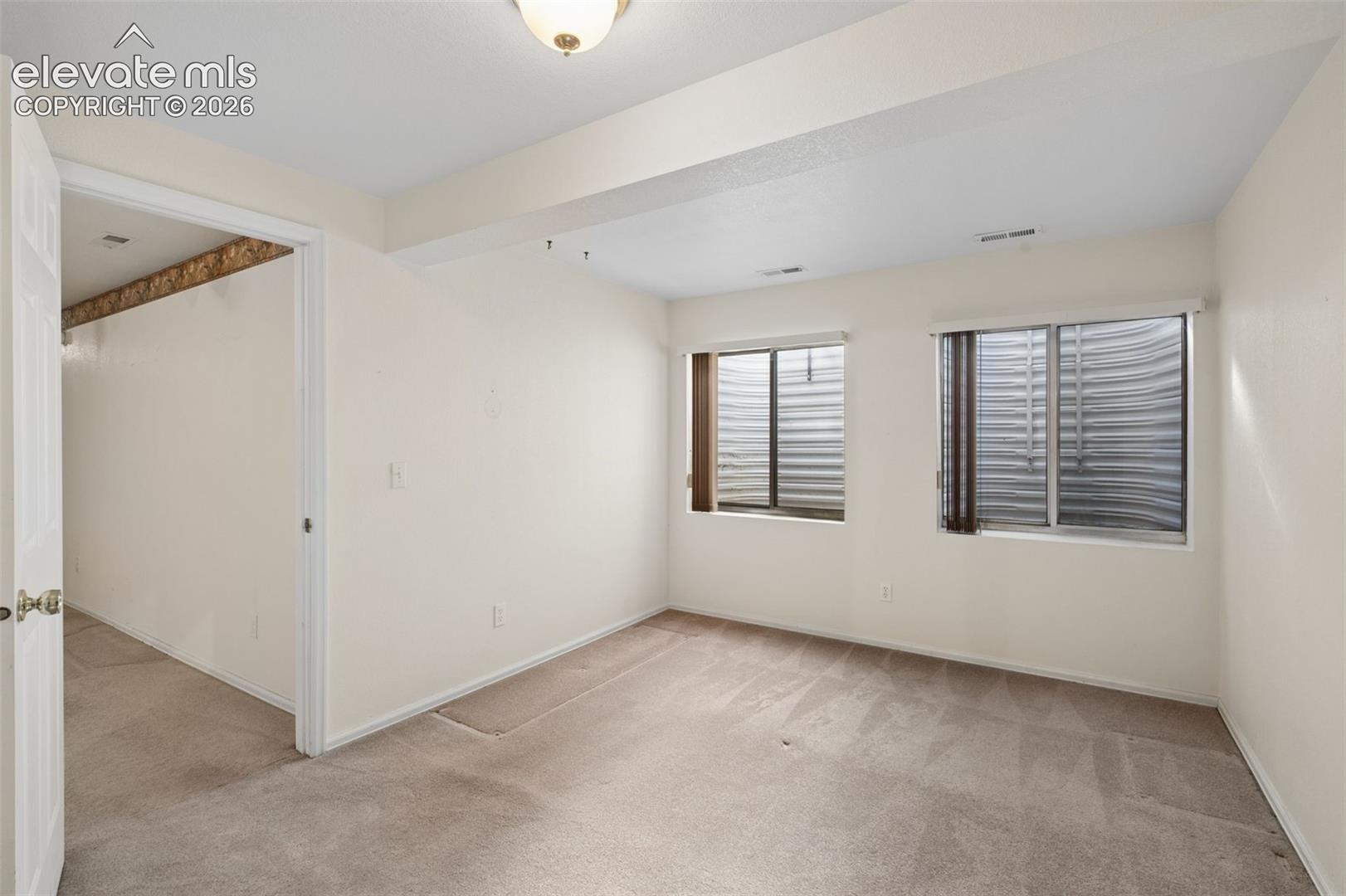 Room featuring neutral wall-to-wall carpeting, two egress windows with metal window wells, and a flush-mount ceiling light fixture