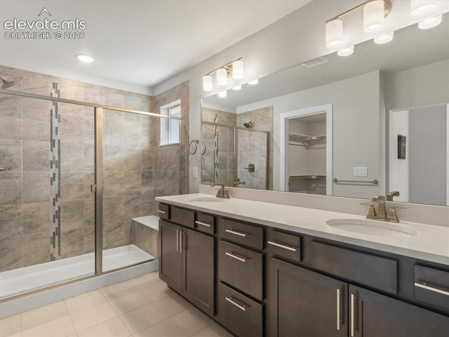 En-suite bath with dual sinks, quartz counter, and oversized tiled shower