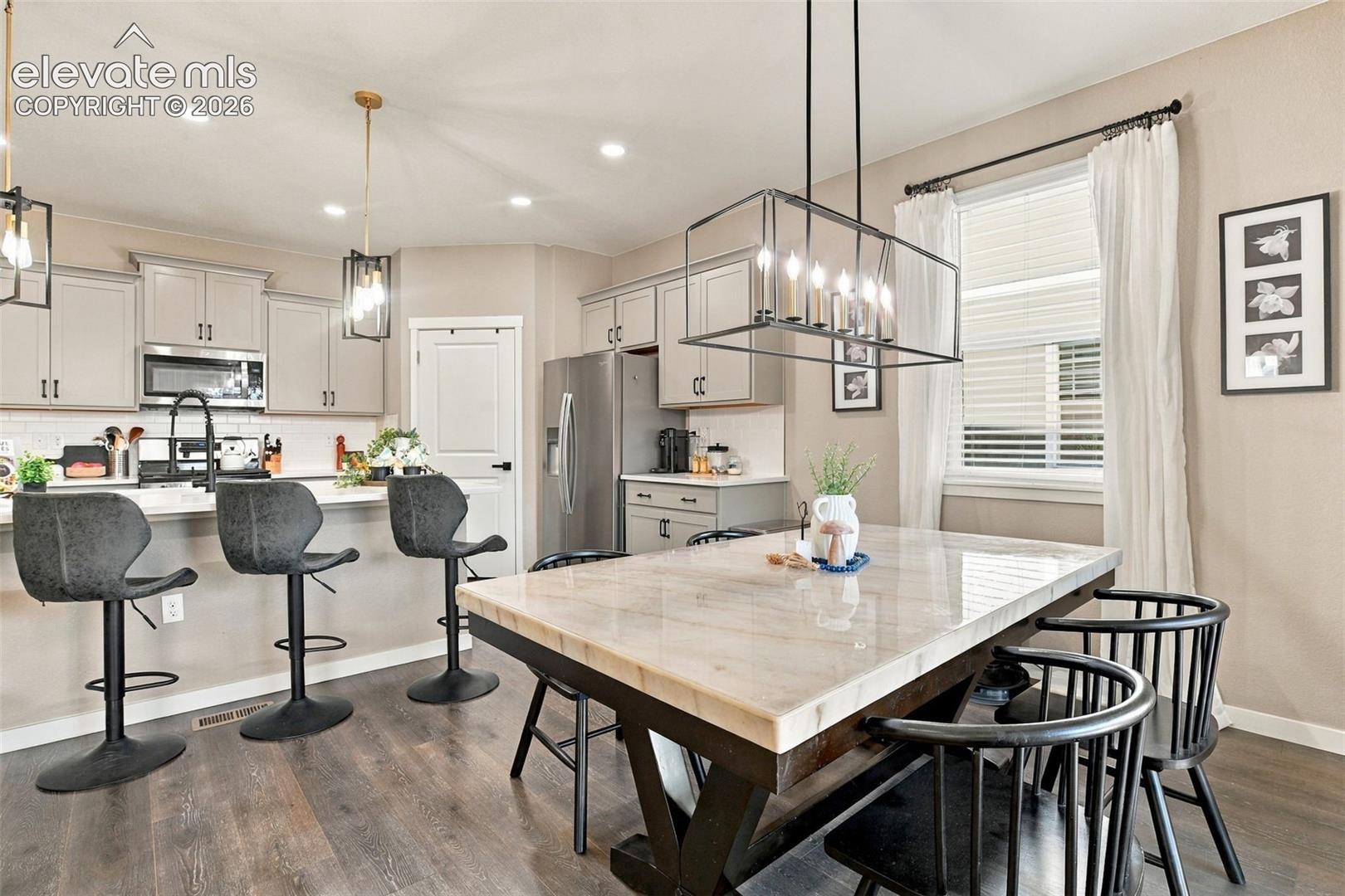 Kitchen featuring neutral-toned cabinetry, stainless steel appliances, a center island with integrated seating, stone-surface counters, and wood-finish flooring