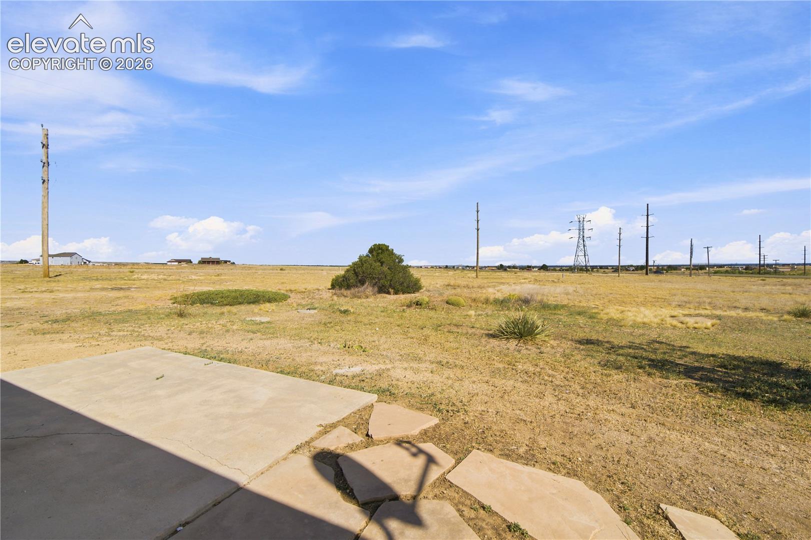 Expansive open land featuring a concrete patio, natural vegetation, and a clear sky