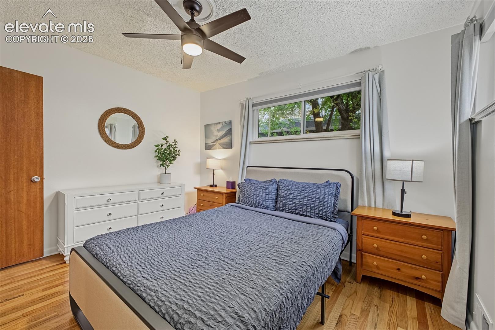 Hardwood flooring, natural light via a horizontal window, ceiling-mounted fan, and interior wood-finish door
