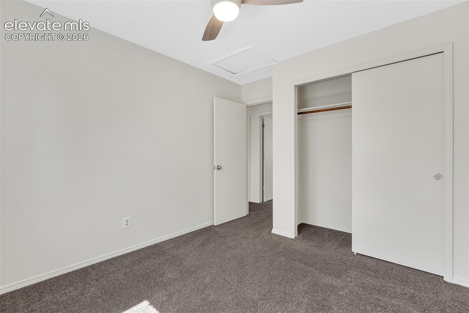 Neutral wall paint, gray carpet flooring, ceiling fan with wood-finish blades, and a built-in closet with sliding doors