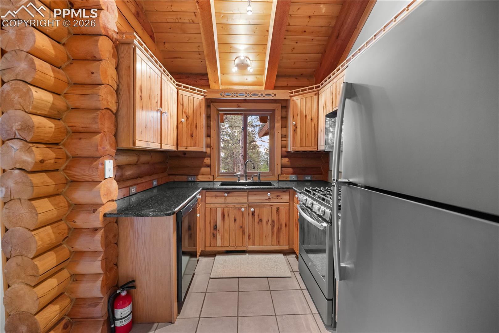 Kitchen featuring stainless steel appliances, wood ceiling, log walls, light tile patterned floors, and dark stone countertops
