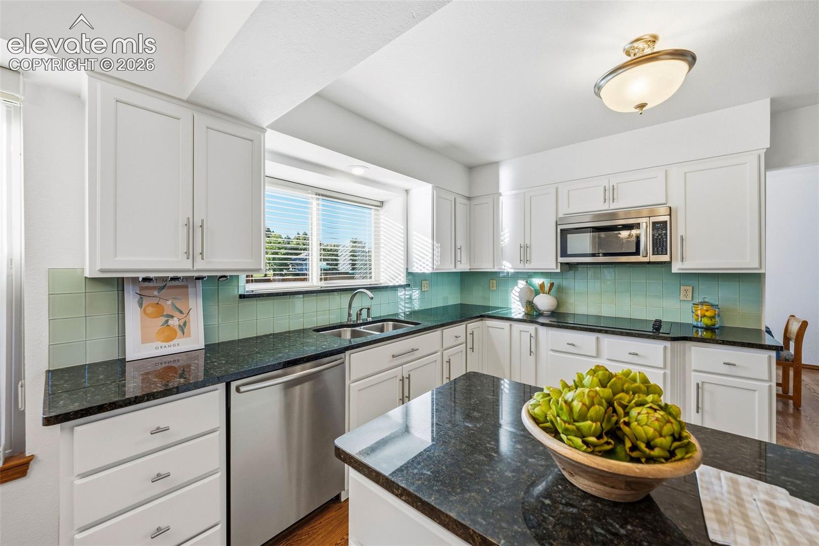 Kitchen featuring white cabinetry, dark stone countertops, stainless steel appliances, a center island, and a light-toned tile backsplash