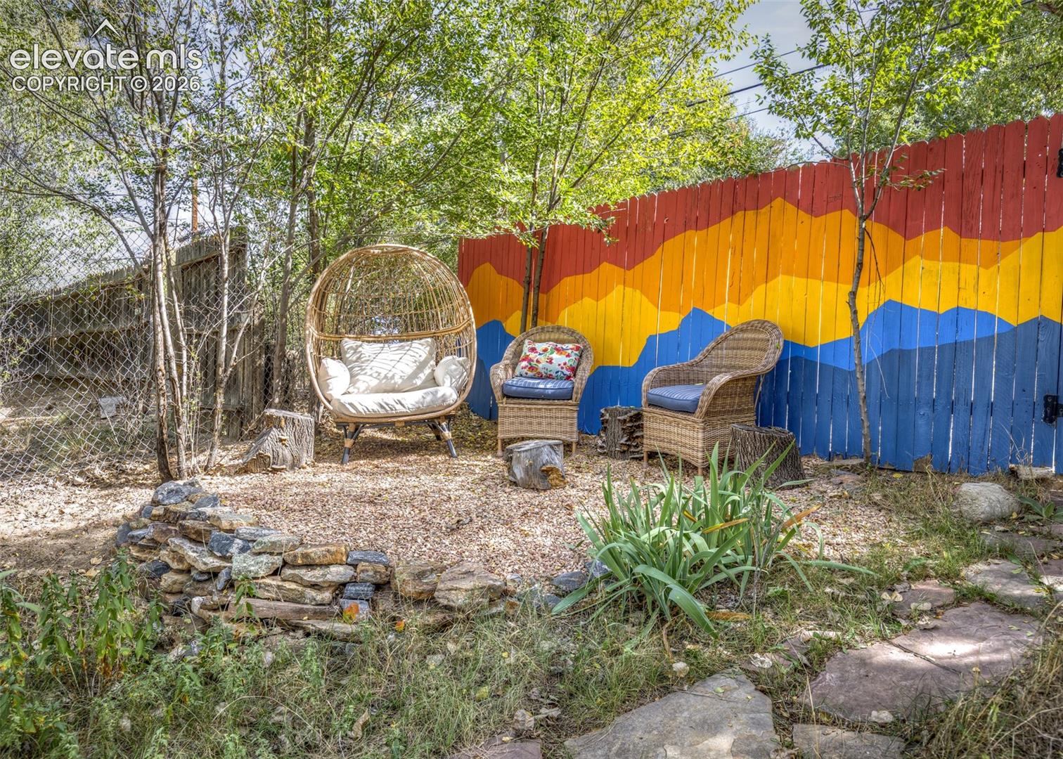 Landscaped outdoor area featuring a stone border, flagstone path, and a colorful painted privacy fence
