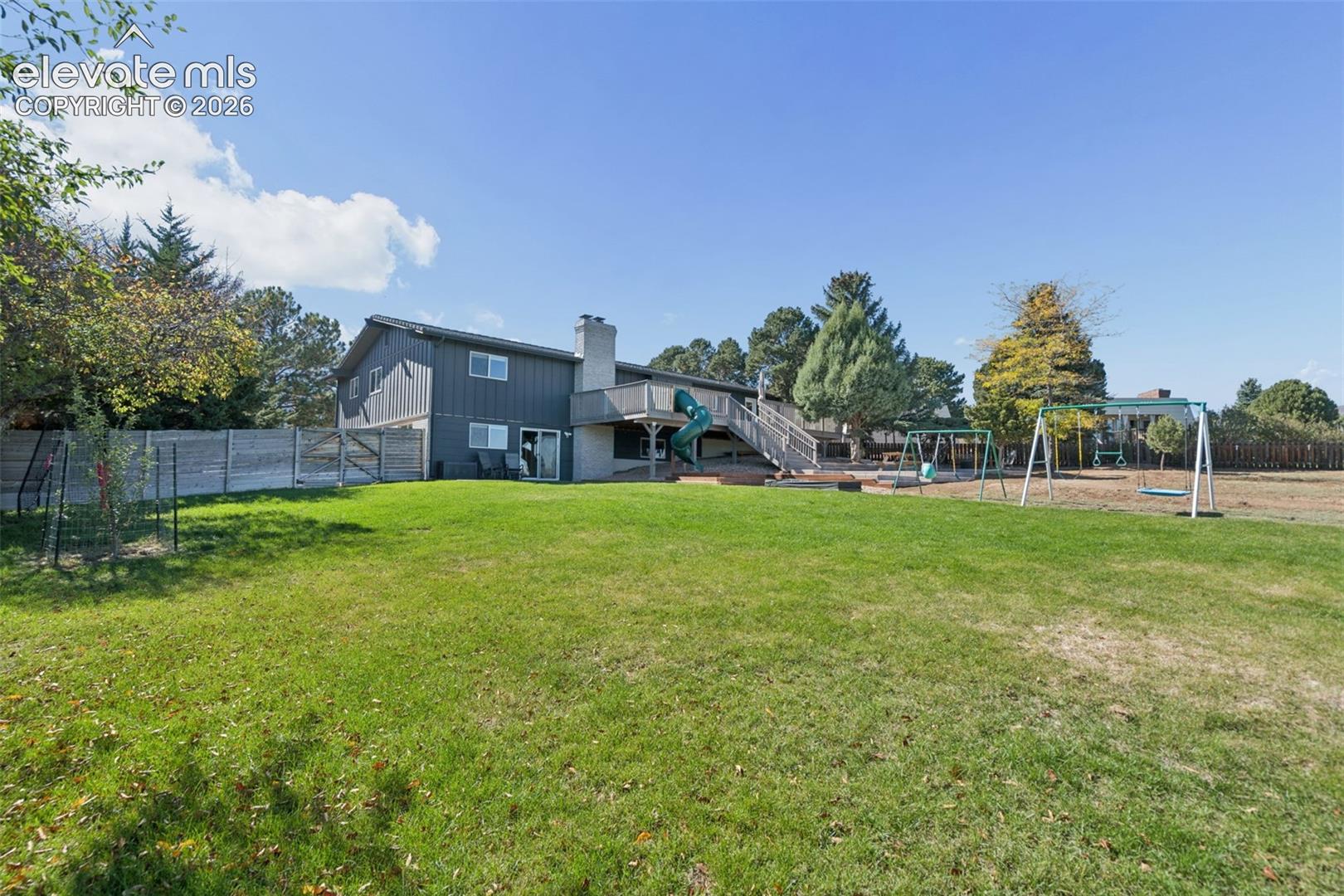 Expansive backyard featuring a multi-level deck, exterior chimney, privacy fencing, and mature trees