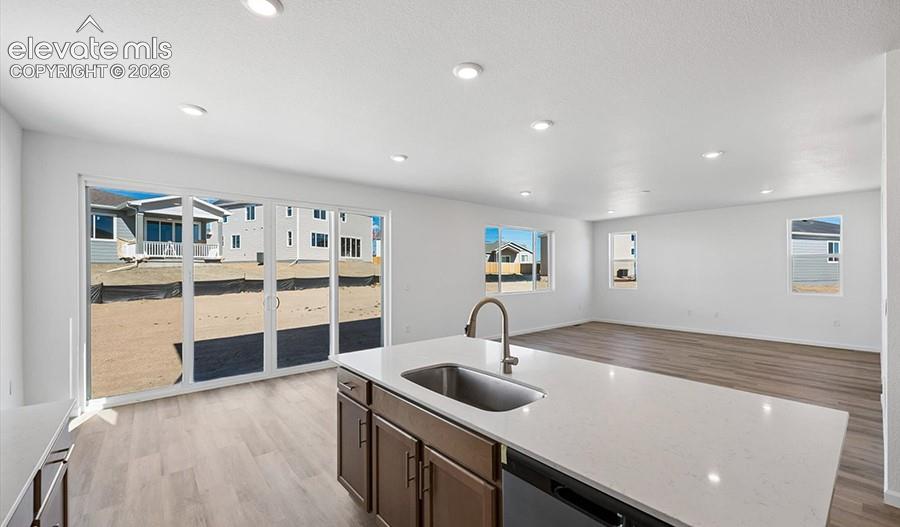 Kitchen island featuring a stone-composite countertop, undermount stainless steel sink, and gooseneck faucet, set against wood-finish flooring, recessed lighting, and expansive sliding glass doors