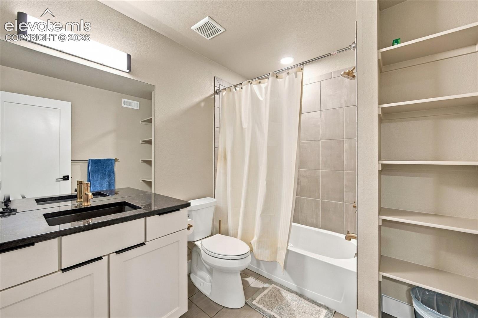 Vanity with dark stone top, built-in shelving, and tub-shower combination with tiled surround