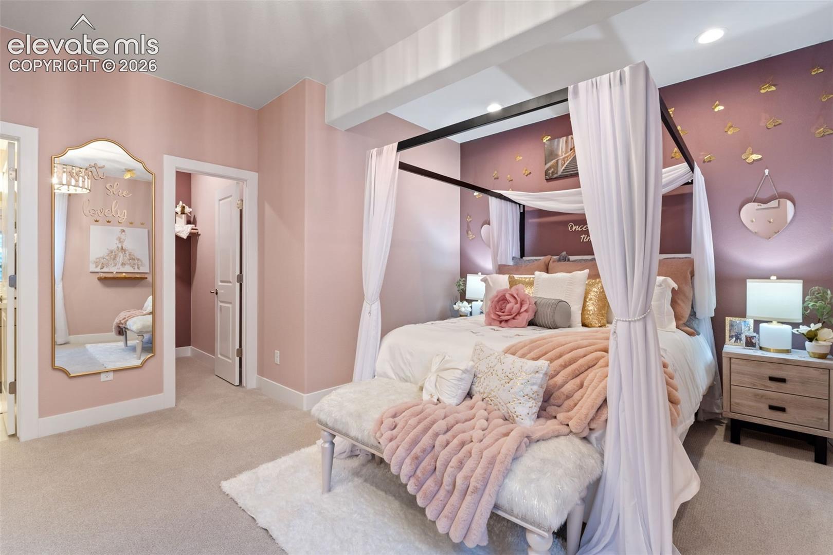 Bedroom featuring neutral carpeting, recessed lighting, a decorative wall-mounted mirror with an arched top, and an interior doorway leading to a walk-in closet