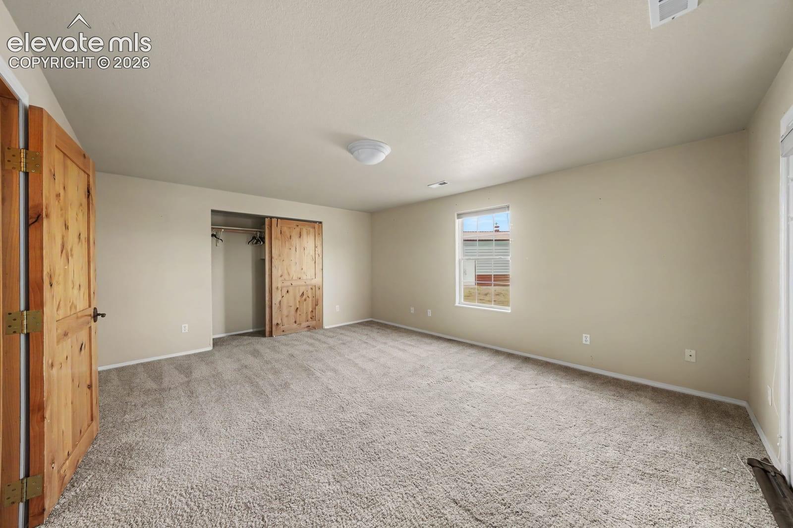 Interior space featuring neutral-toned carpeting, natural wood-finish interior doors, a sliding closet door, and a single-pane window