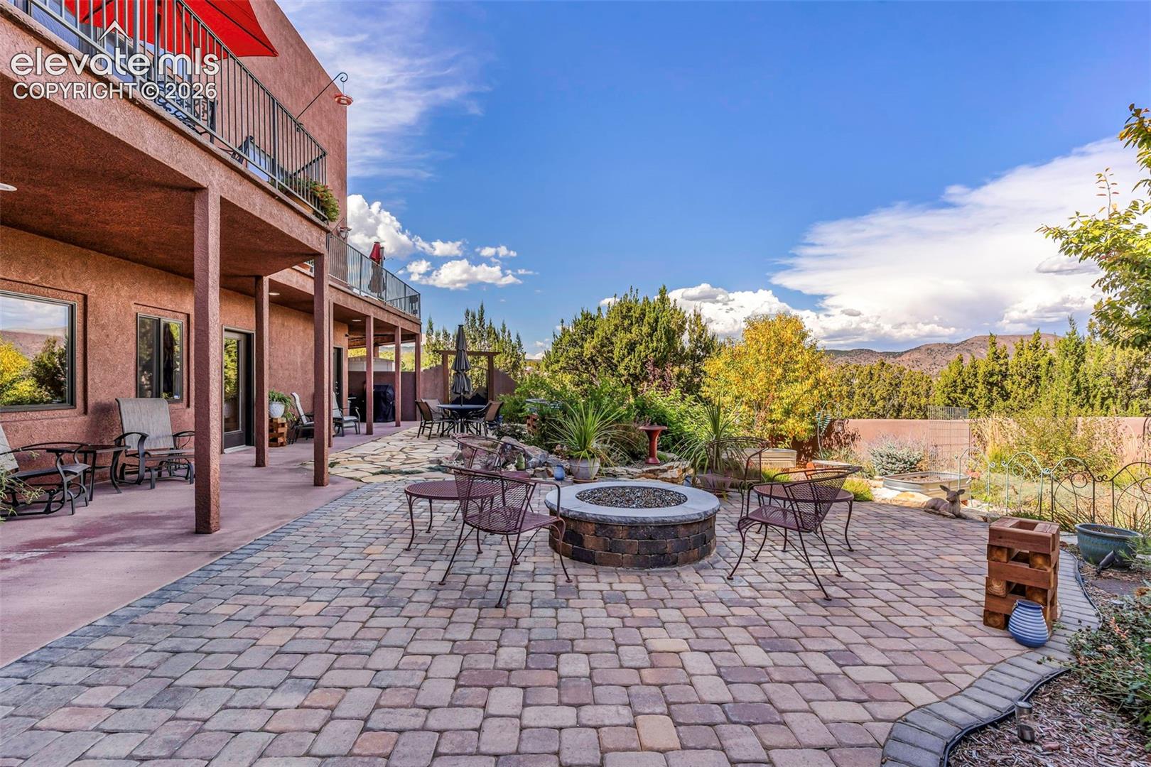 Stucco exterior featuring a covered patio, circular stone fire pit, and expansive paver hardscaping