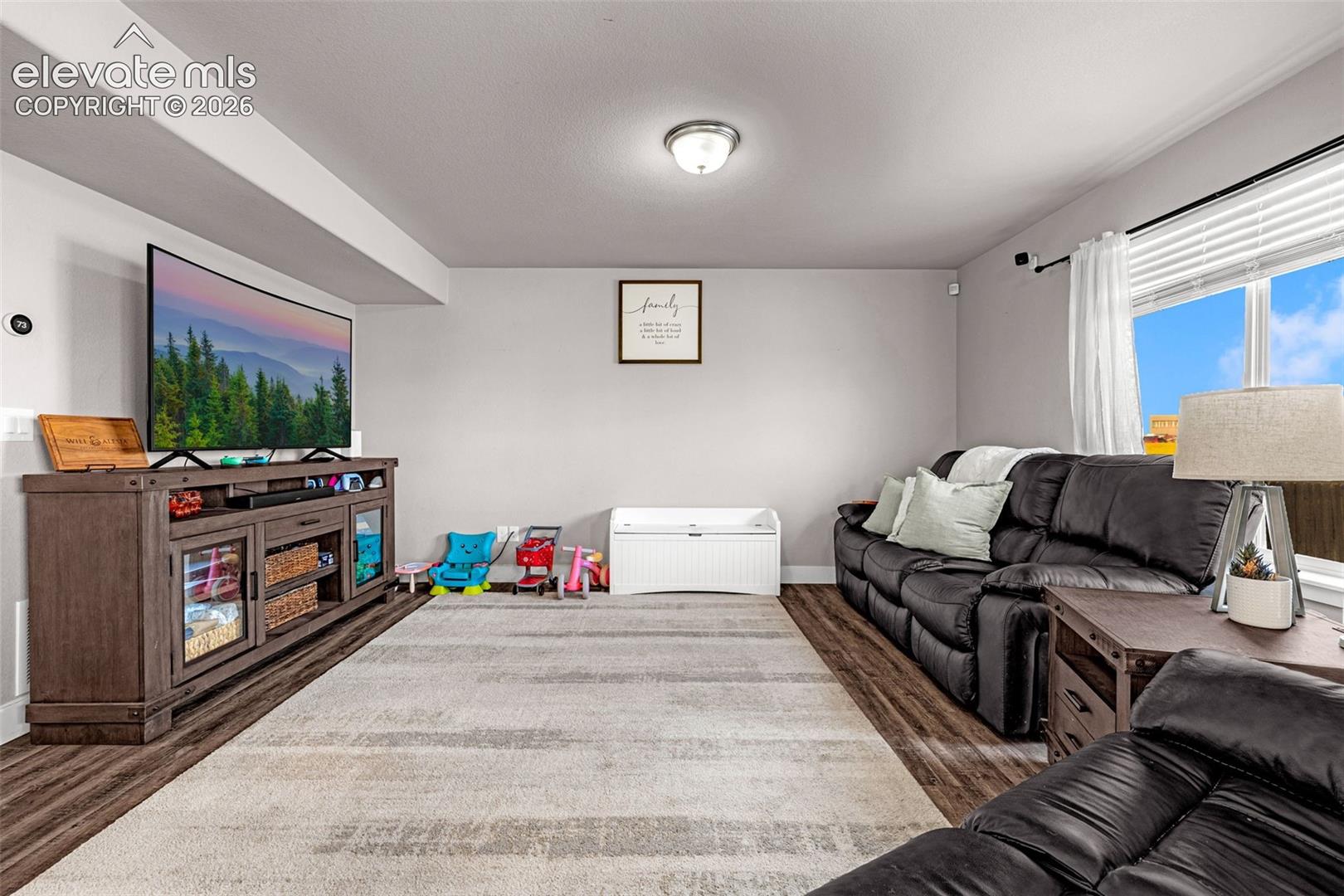 Spacious room featuring wood-finish flooring, light gray walls, and a large window with white blinds