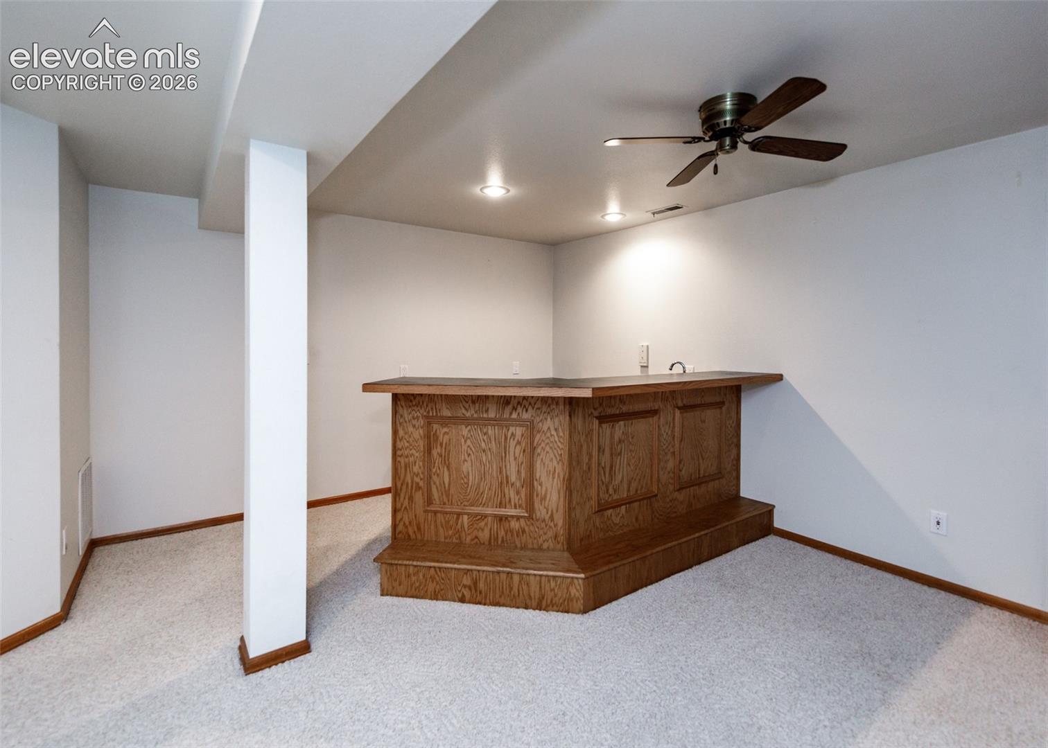 Built-in wood-paneled bar with a dark countertop, recessed lighting, and a ceiling fan