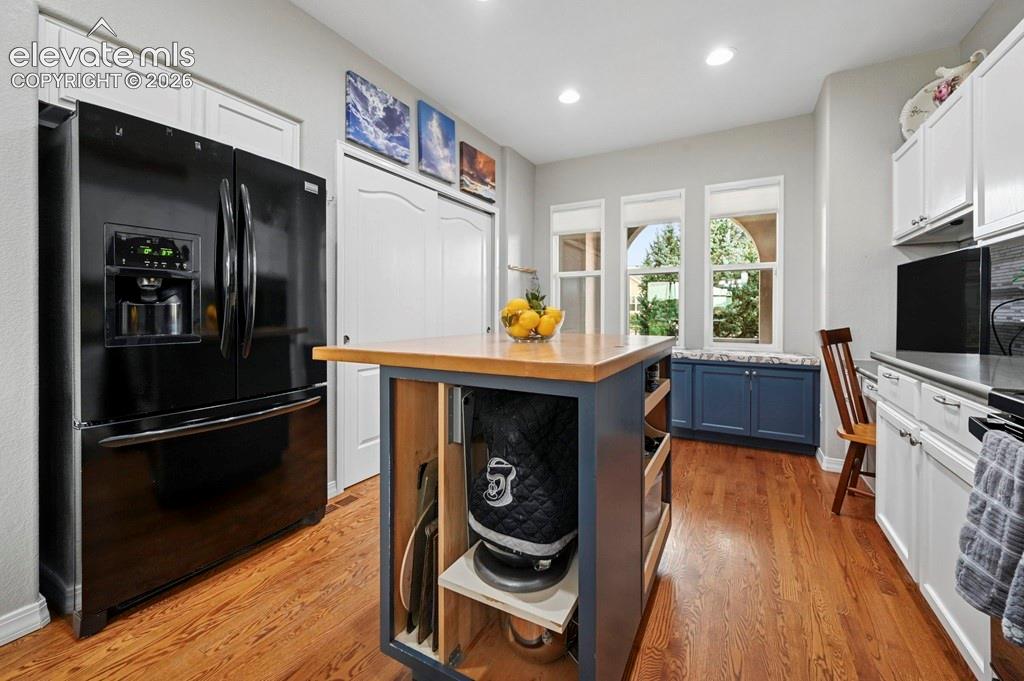Hardwood flooring, white cabinetry, dark countertop, kitchen island with wood top, and recessed lighting