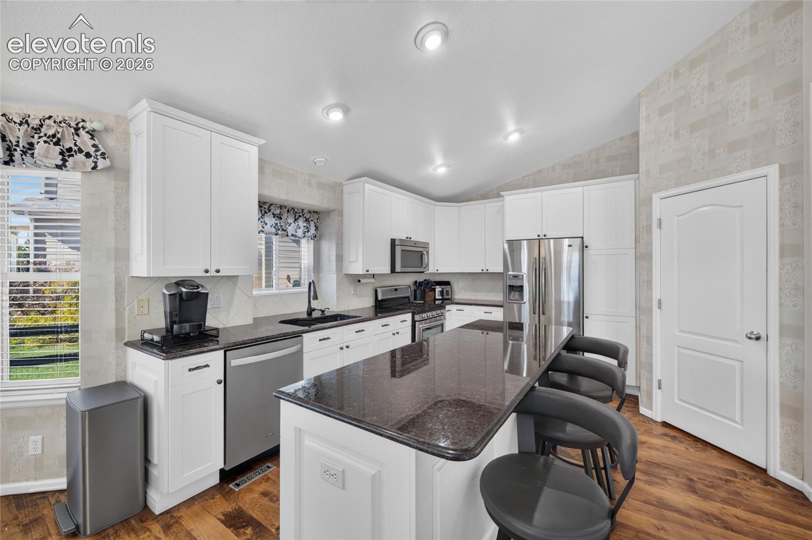 Kitchen featuring white cabinetry, an expansive center island with stone-finish countertops, stainless steel appliances, recessed ceiling lighting, and wood-finish flooring
