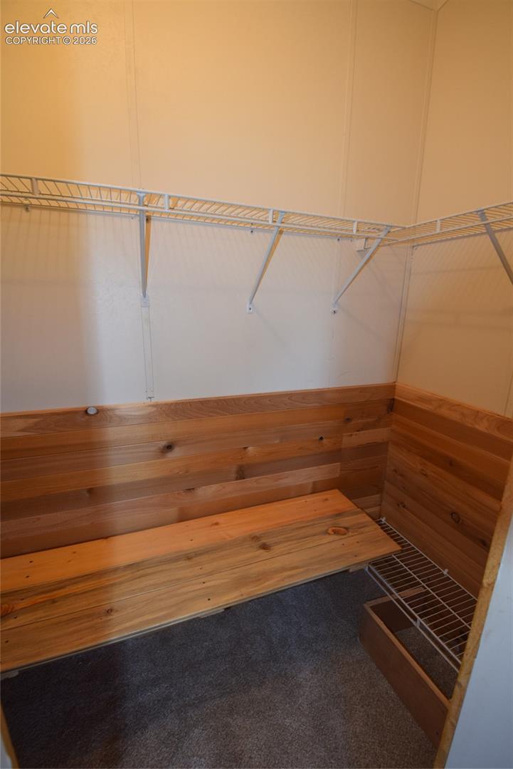 Wood-paneled storage nook with integrated bench seating, wire shelving, and carpeted flooring