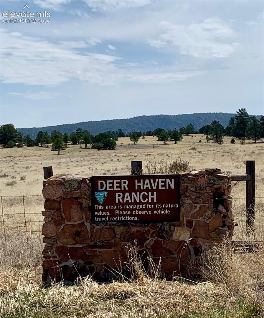 Stone-pillar signage structure with open terrain, mature trees, and mountain backdrop