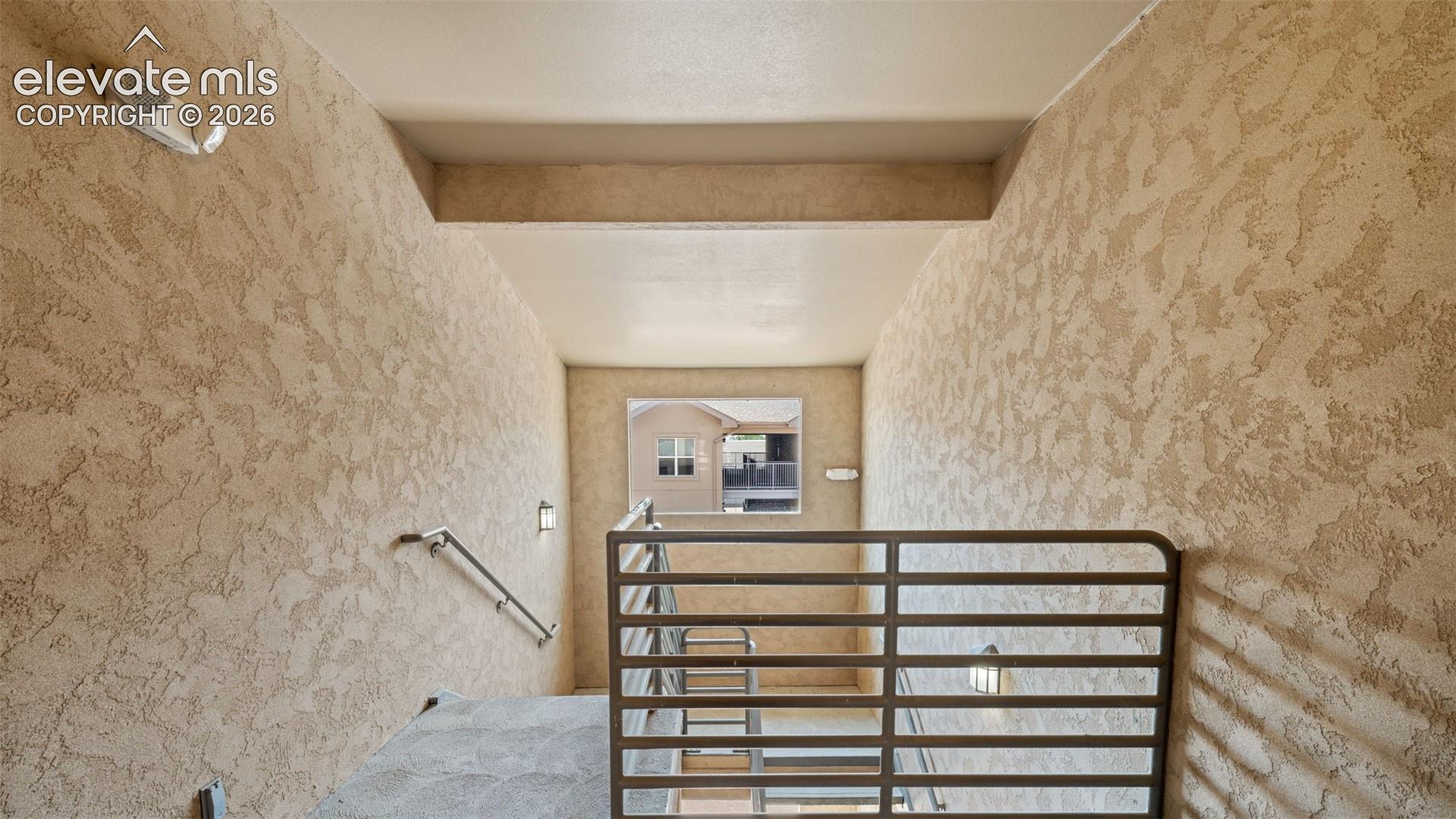 Stairwell with textured stucco walls, metal railings, and integrated wall sconces