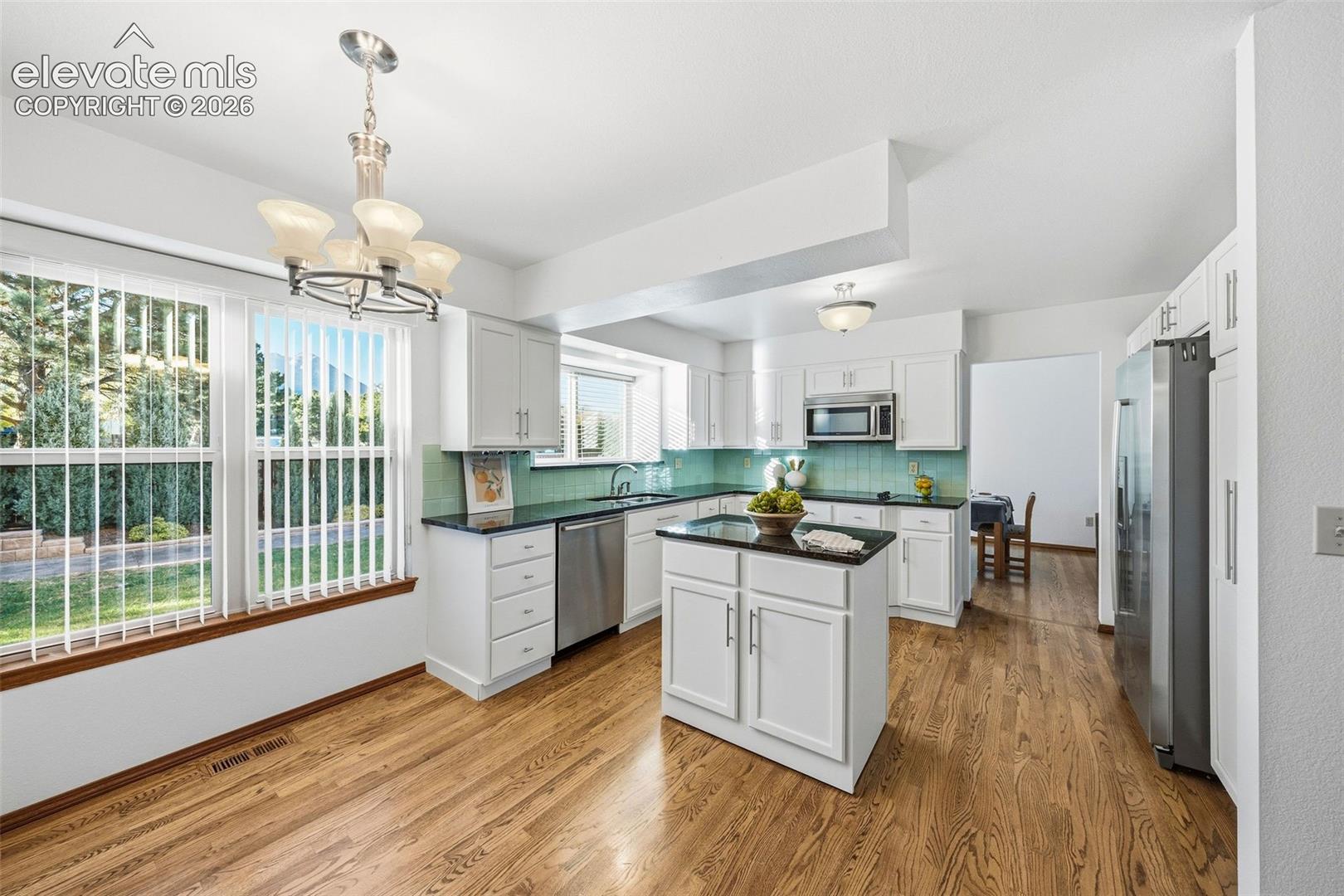 Kitchen featuring white cabinetry, center island, dark stone-finish countertops, stainless steel appliances, and wood-finish flooring