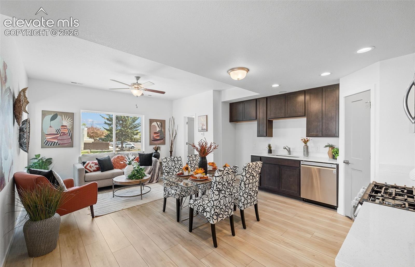 Open-concept interior featuring light wood-finish flooring, dark-toned cabinetry, stainless steel dishwasher, flush-mount ceiling lighting, and a ceiling fan