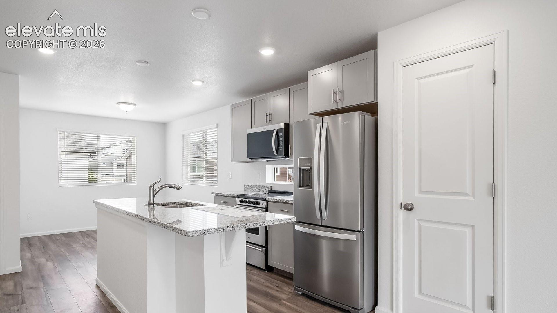 Kitchen featuring a center island with sink, stainless steel appliances, recessed lighting, wood-finish flooring, and light gray cabinetry
*photos of a model home*