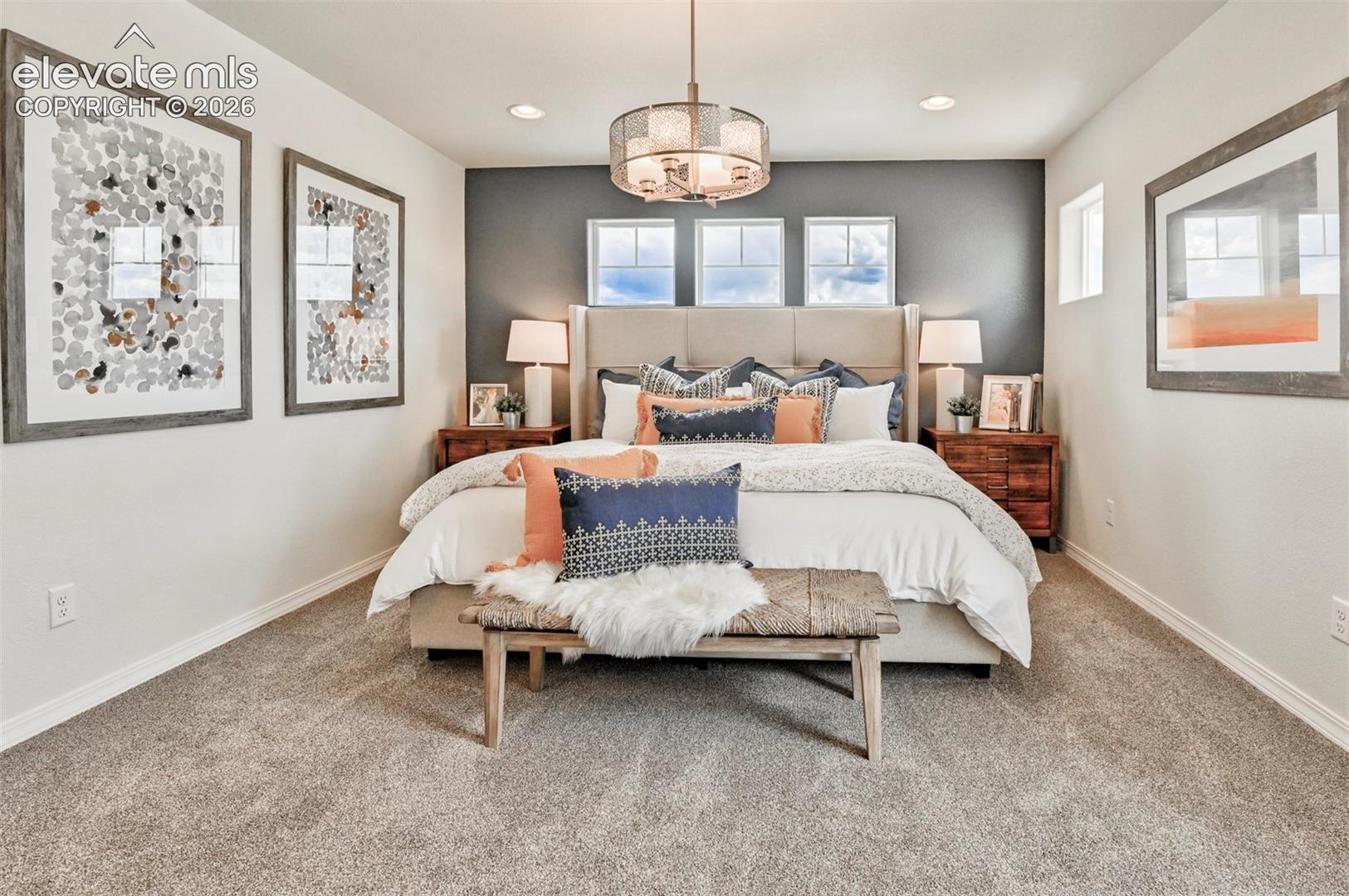 Primary bedroom with upholstered headboard, three small windows above bed, dark accent wall, and pendant chandelier