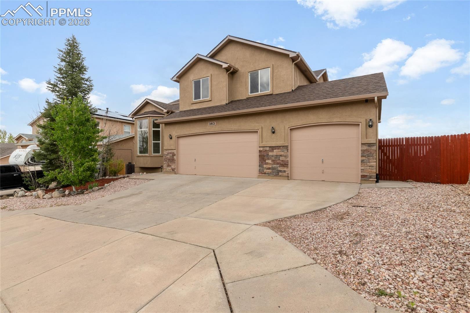 Stucco exterior featuring stone veneer accents, a three-car garage, and a concrete driveway