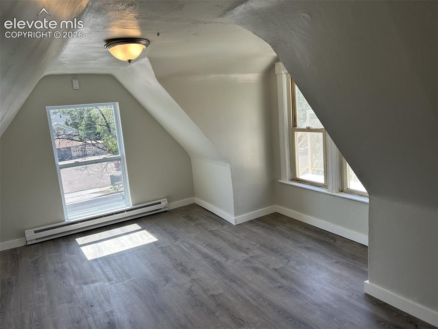 Wood-finish flooring, two windows, baseboard heating, recessed lighting, and sloped ceilings