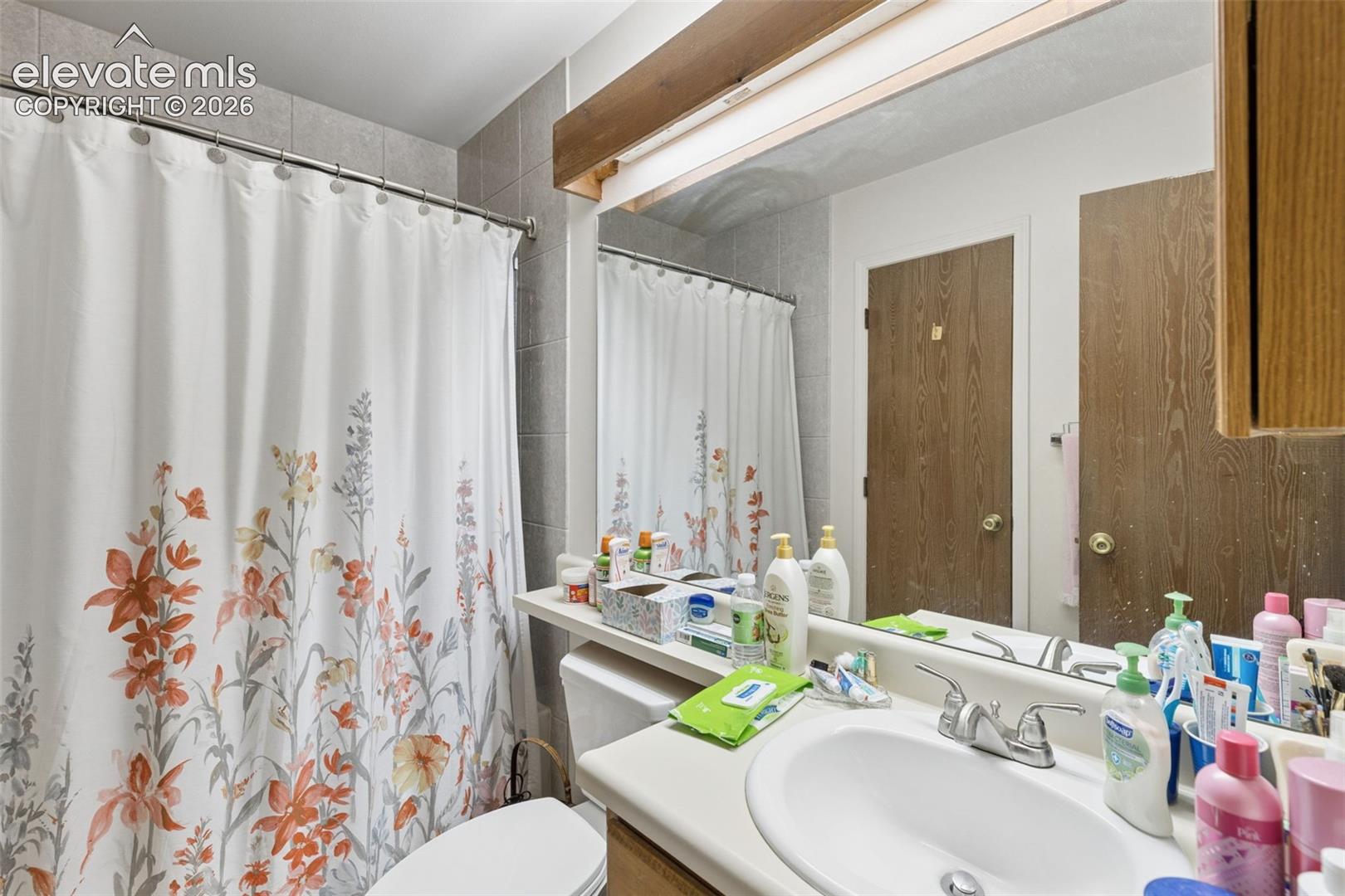 Bathroom featuring a full-width vanity mirror with a wood-trimmed light fixture, integrated sink with polished chrome hardware, and a tile-surround shower area