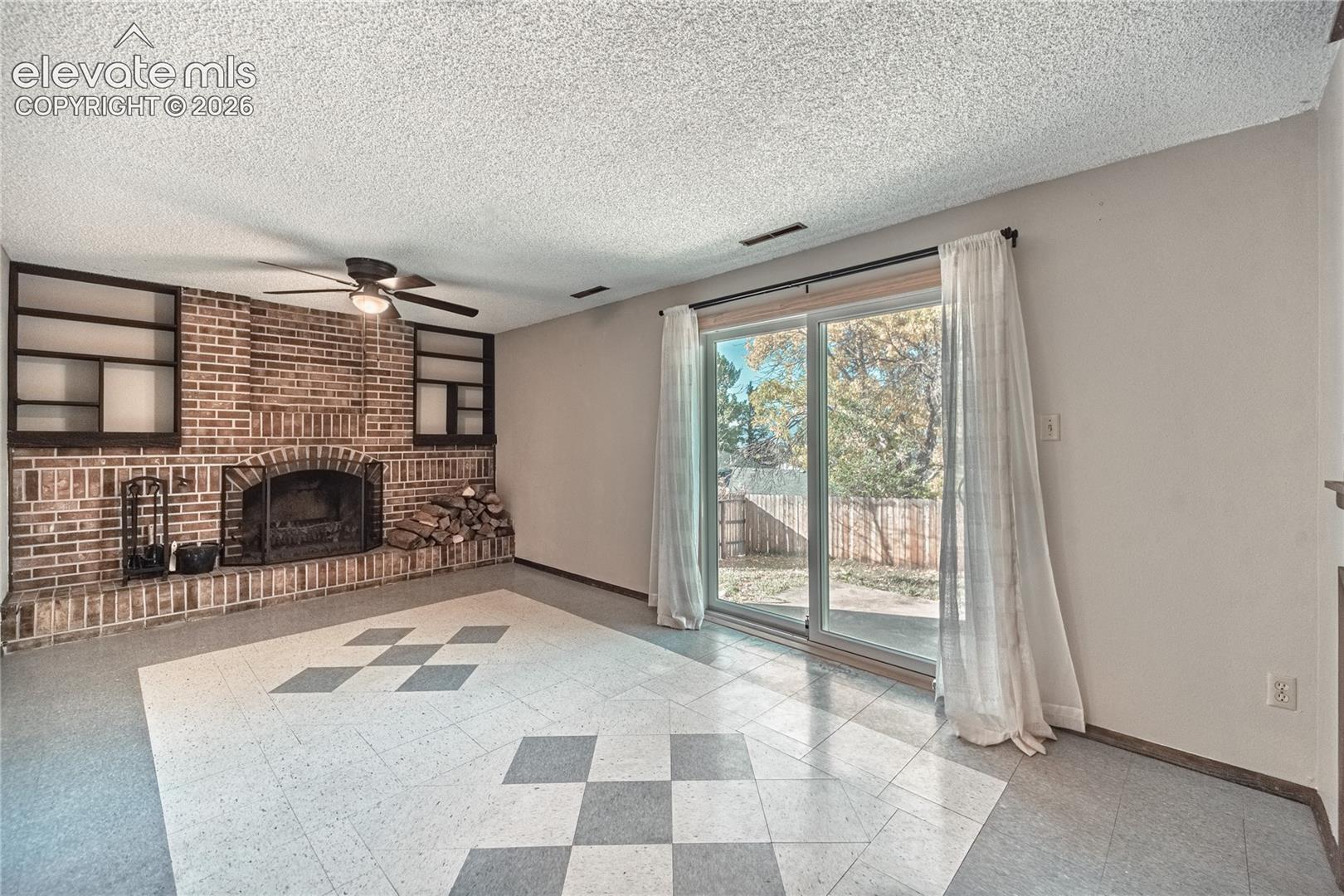 Floor-to-ceiling brick fireplace with built-in flanking shelving, sliding glass door, and patterned tile flooring