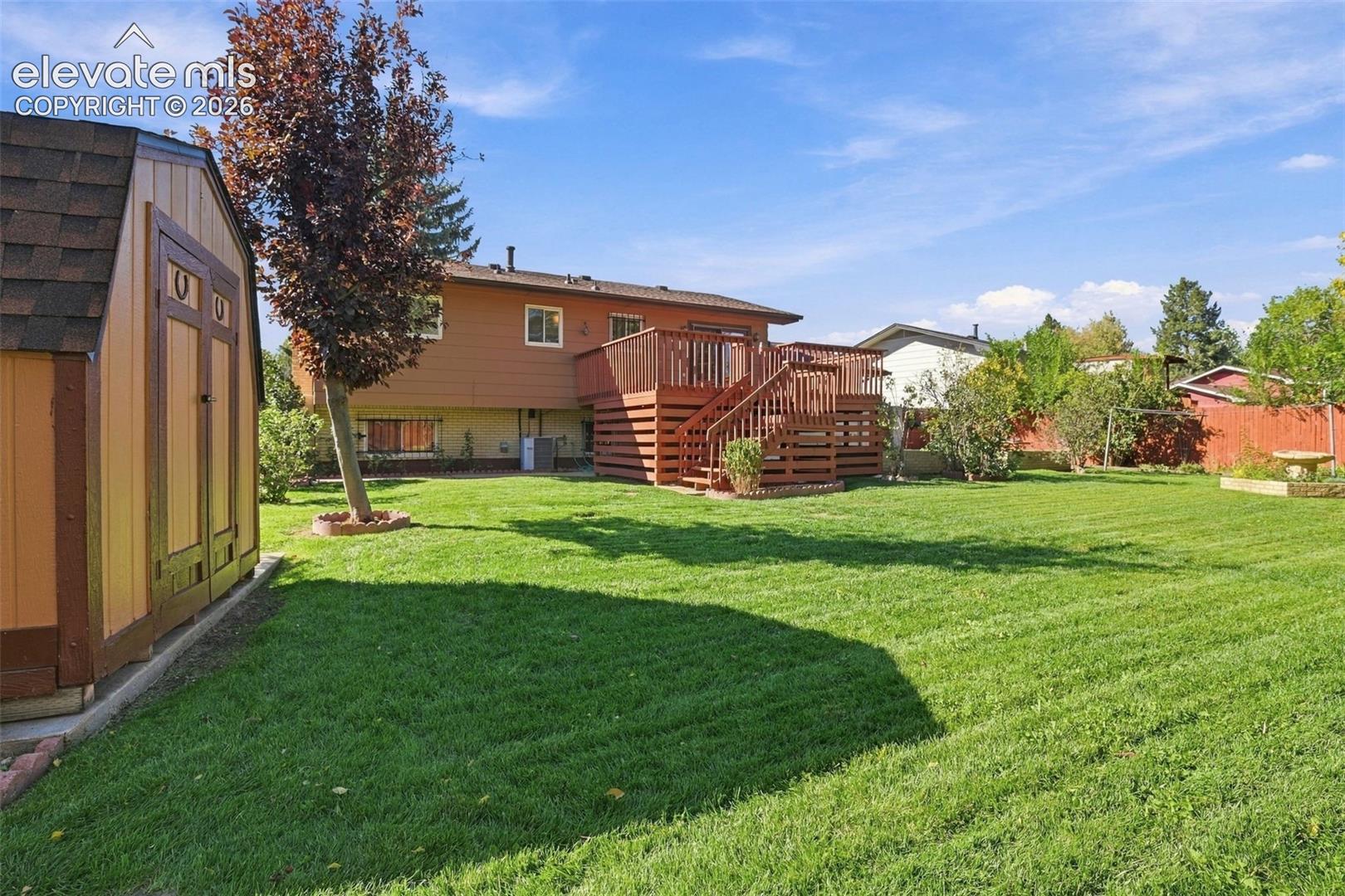Backyard featuring a wood-finish storage shed, elevated wood deck with stairs, manicured lawn, and perimeter wood fencing