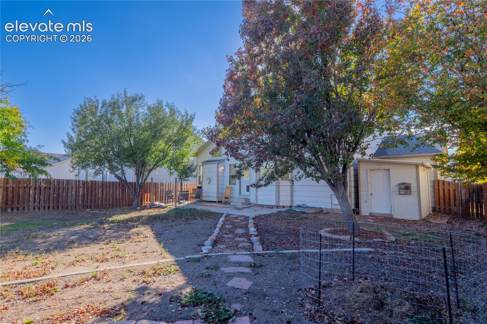 A fenced backyard with mature trees, established landscaping, and a winding stone pathway.