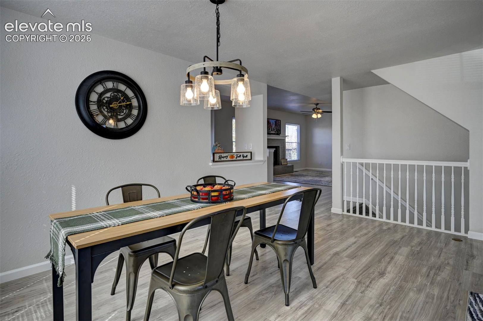 Wood-finish flooring, multi-light wagon wheel chandelier, and white staircase railing with vertical balusters