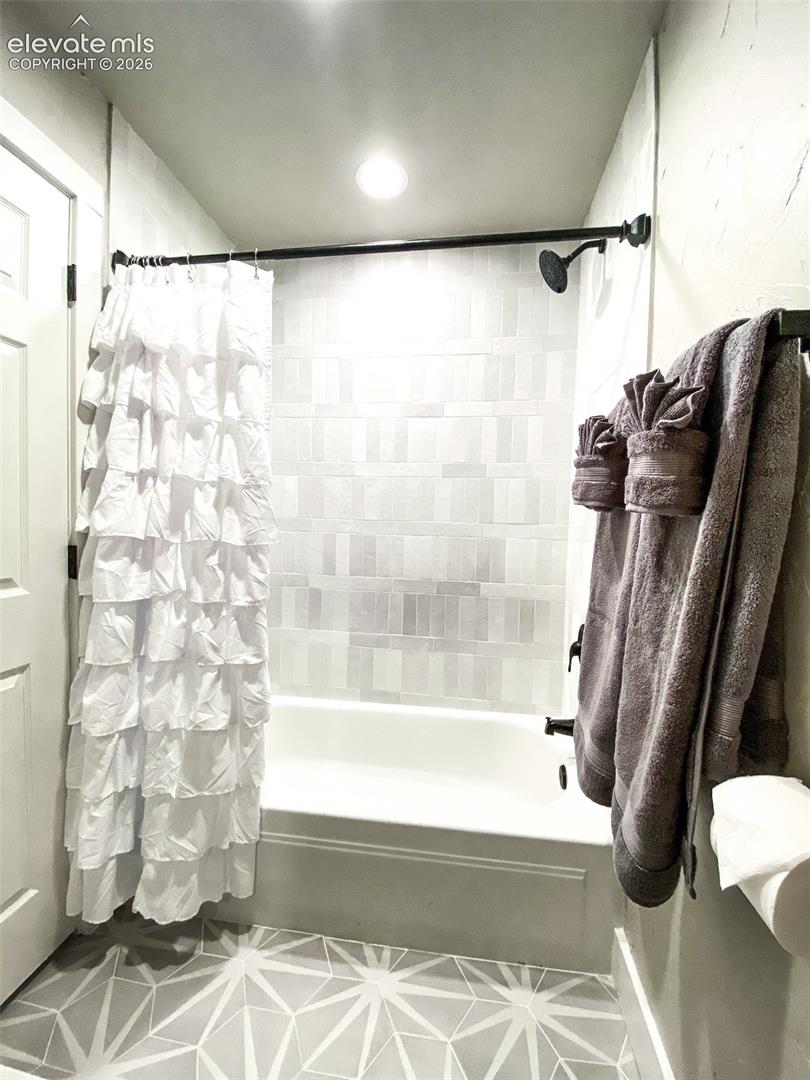 Bathroom featuring a white bathtub, gray rectangular tile surround, matte black shower fixtures, and geometric pattern floor tiling