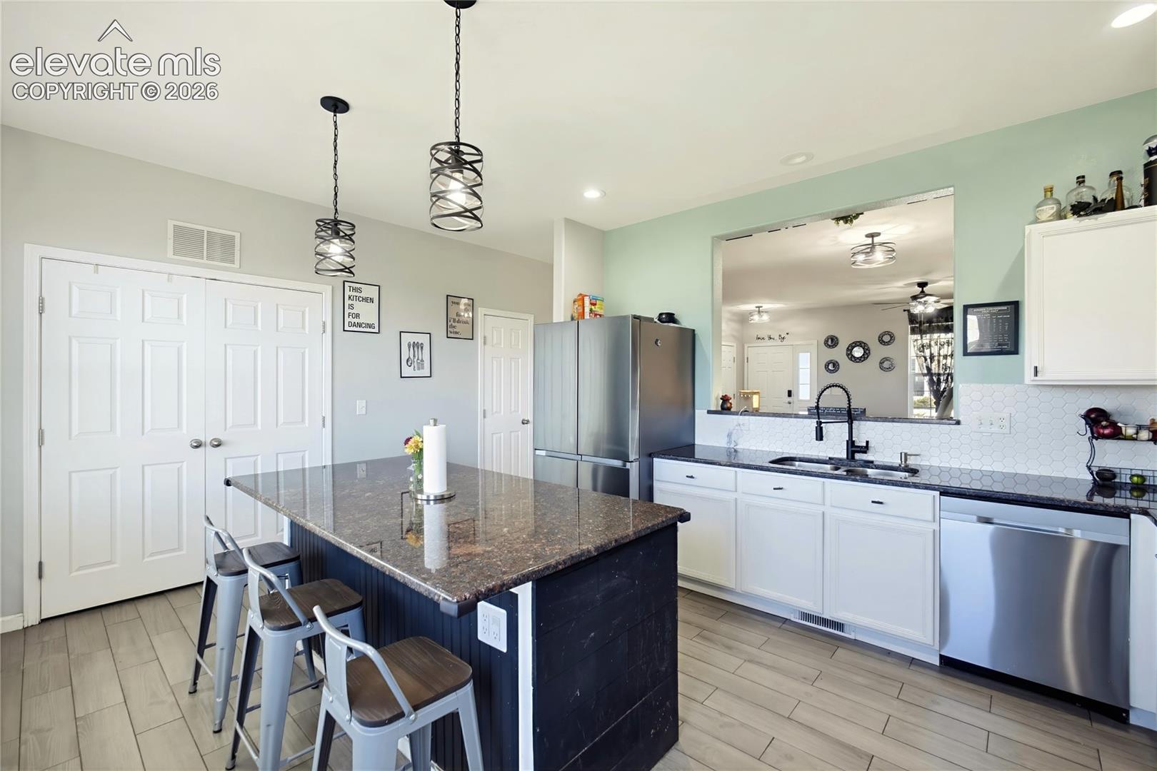 Kitchen featuring a central island with a stone countertop, white cabinetry with dark hardware, stainless steel appliances, a white tile backsplash, and light wood-finish flooring