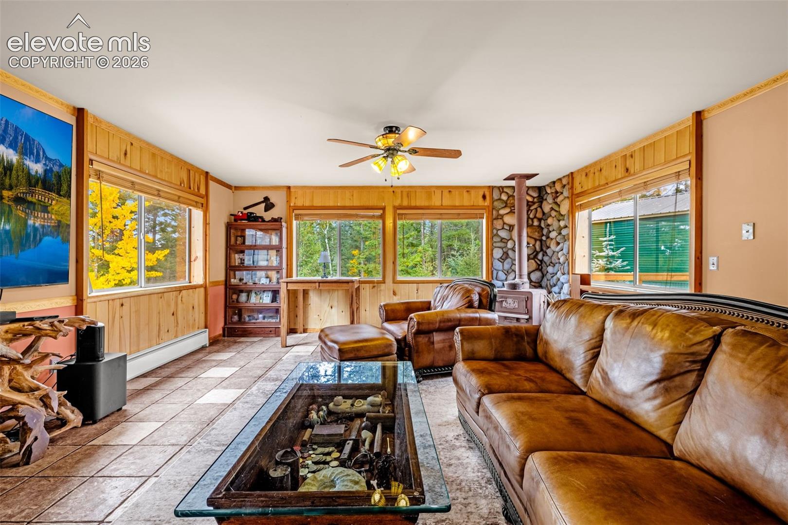 Interior space featuring wood-panelled walls, floor-to-ceiling stone fireplace, ceramic tile flooring, and multiple windows