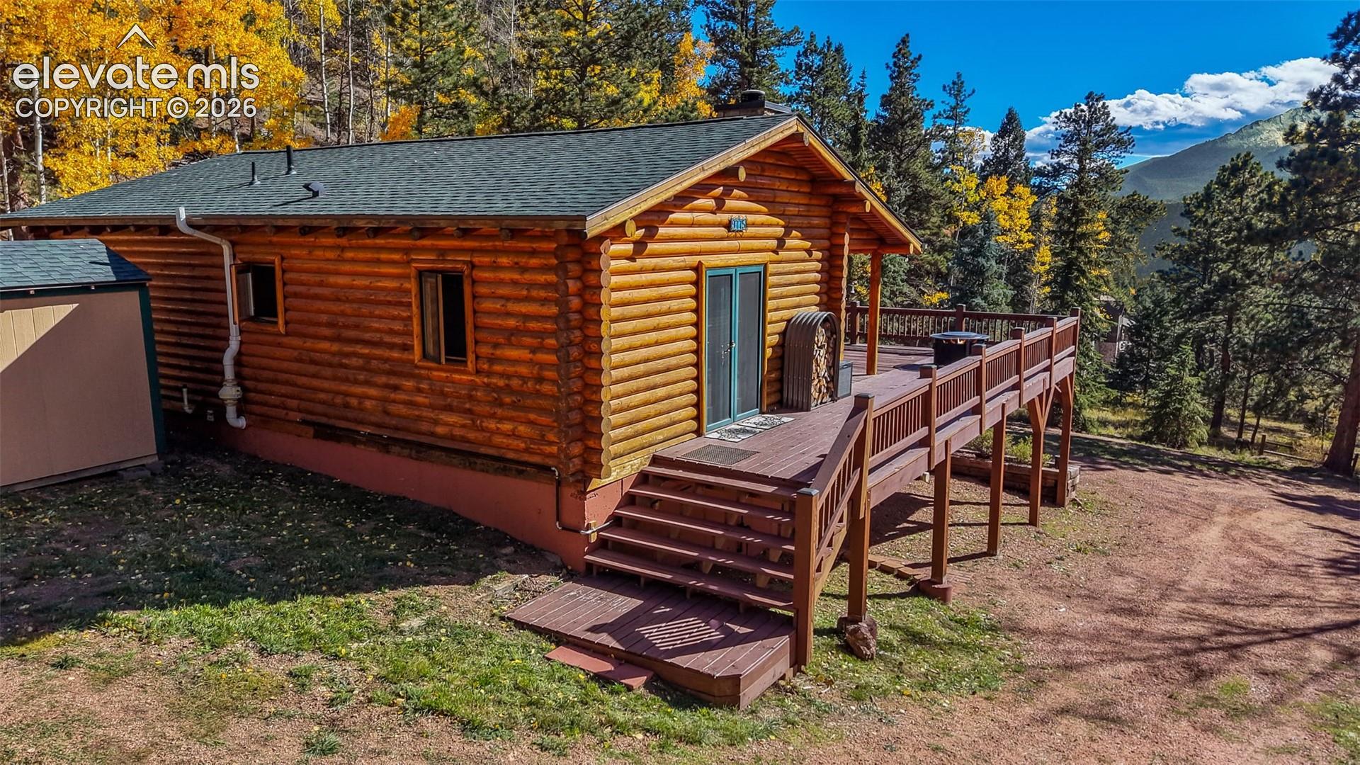 Log cabin exterior featuring horizontal log construction, a green shingle roof, and a tiered wooden deck with railing