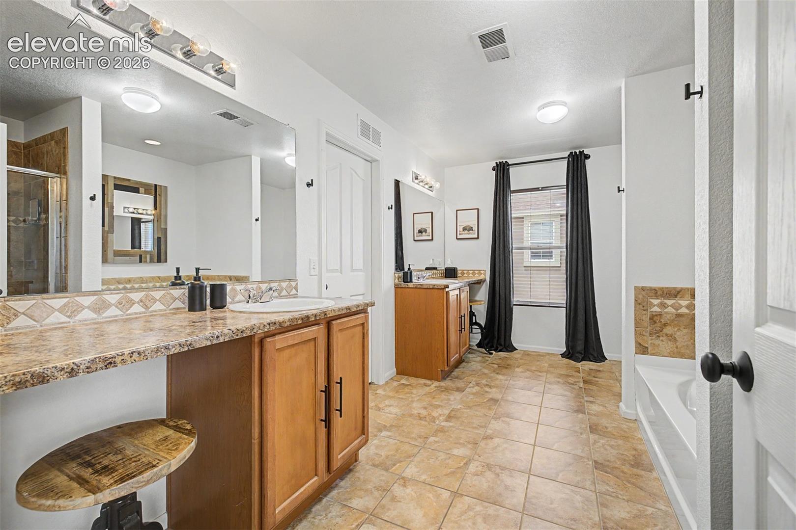 The primary bathroom is built for two, with dual vanity stations, granite countertops, warm wood cabinetry, and a sprawling layout that makes even the busiest mornings feel unhurried.