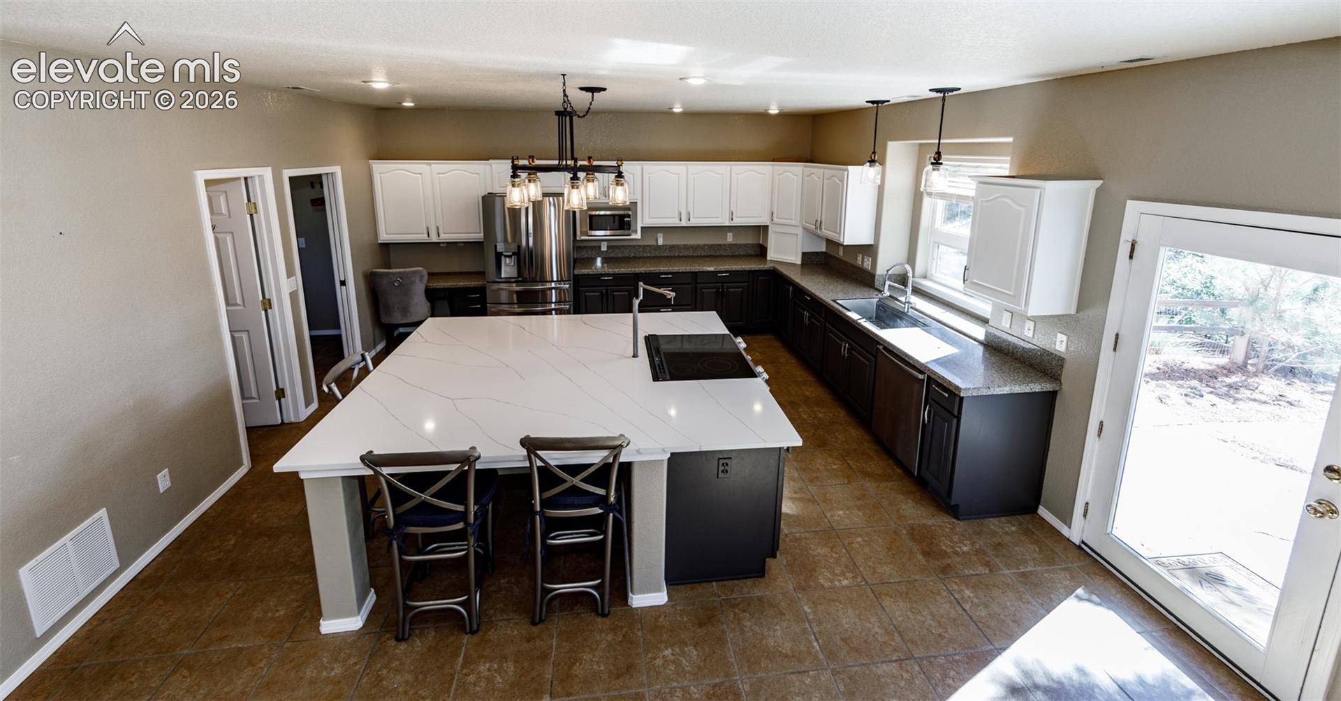 Kitchen featuring a large central island with light stone-patterned countertop, two-tone cabinetry, recessed lighting, and tile flooring