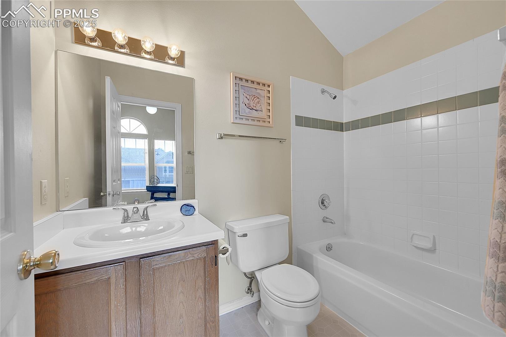 Full adjoining bathroom featuring skylight, vaulted ceiling, tile floor & surround