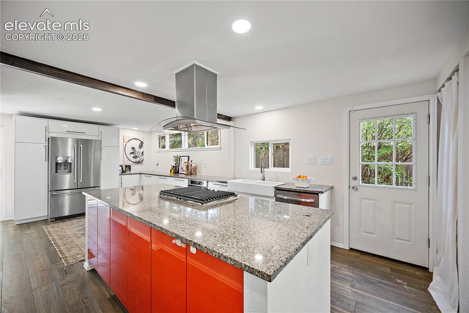 Kitchen featuring a large island with a stone countertop and bright orange cabinetry, a stainless steel refrigerator, and wood-finish flooring