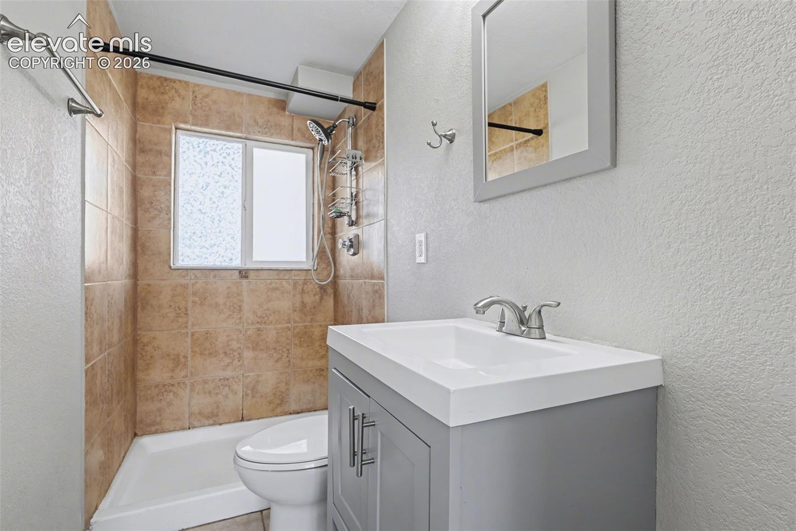 Bathroom featuring a grey vanity with a white rectangular basin, a wall-mounted mirror with a grey frame, tile-surround shower area, and chrome-finish fixtures