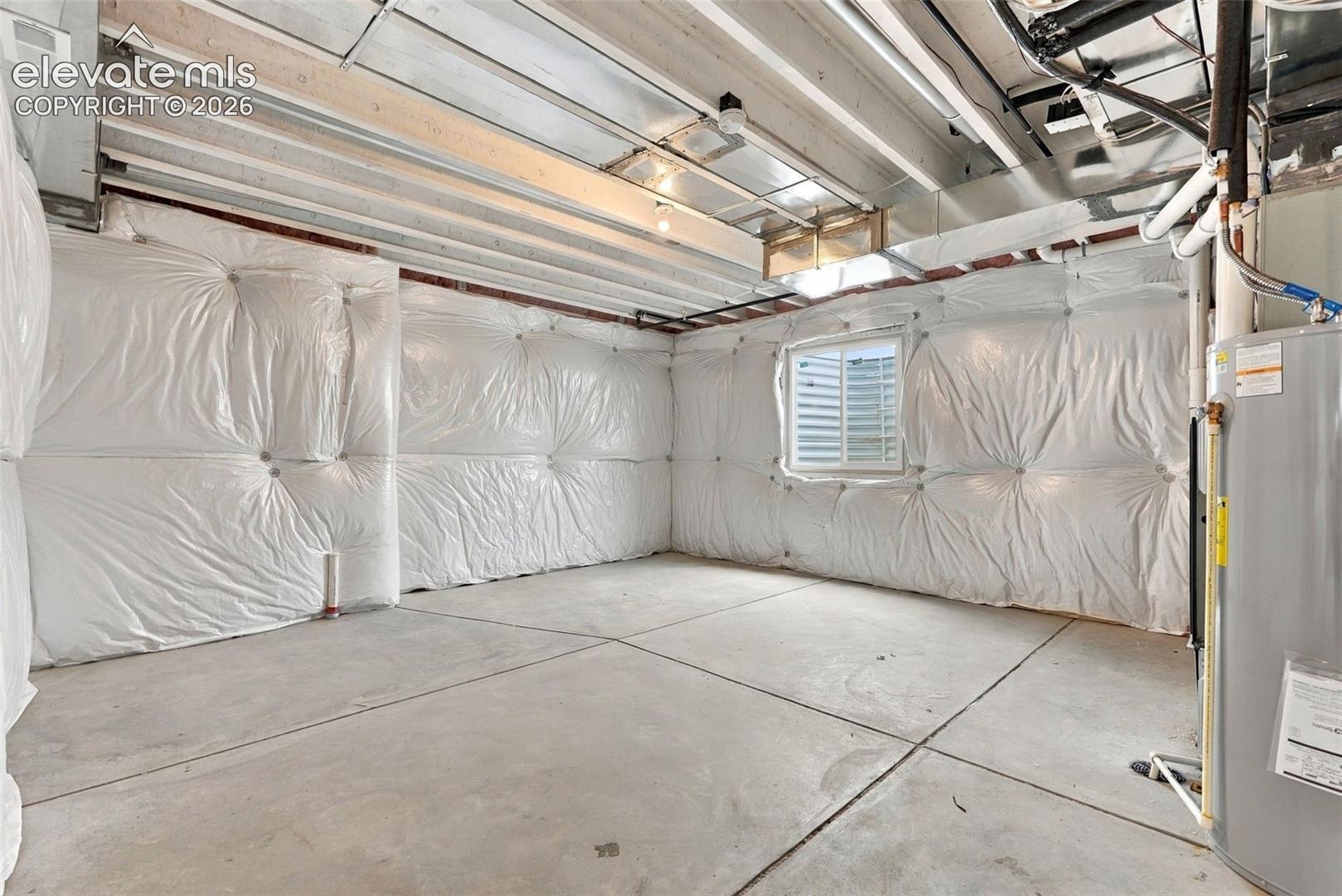 Unfinished lower level featuring concrete flooring, white insulation-wrapped walls, exposed ceiling joists, and a daylight window with a window well