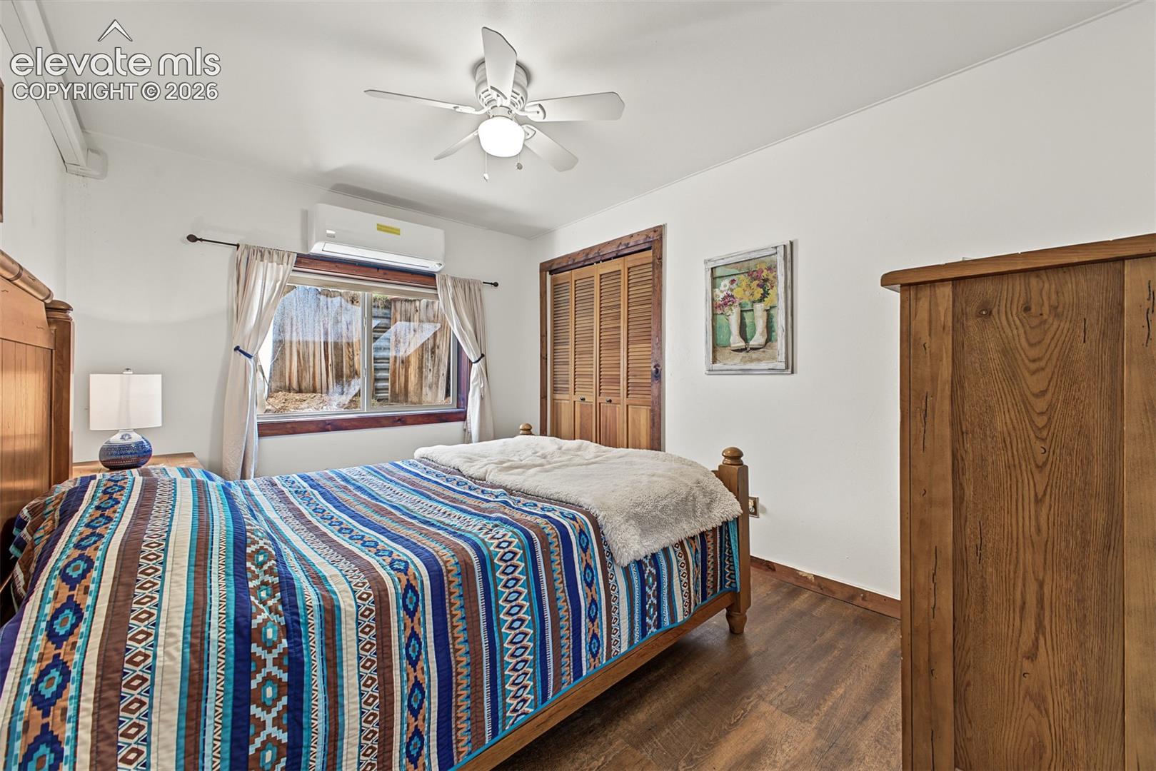 Wood-finish flooring, white walls, louvered bi-fold closet doors, ceiling fan, and a wall-mounted mini-split unit