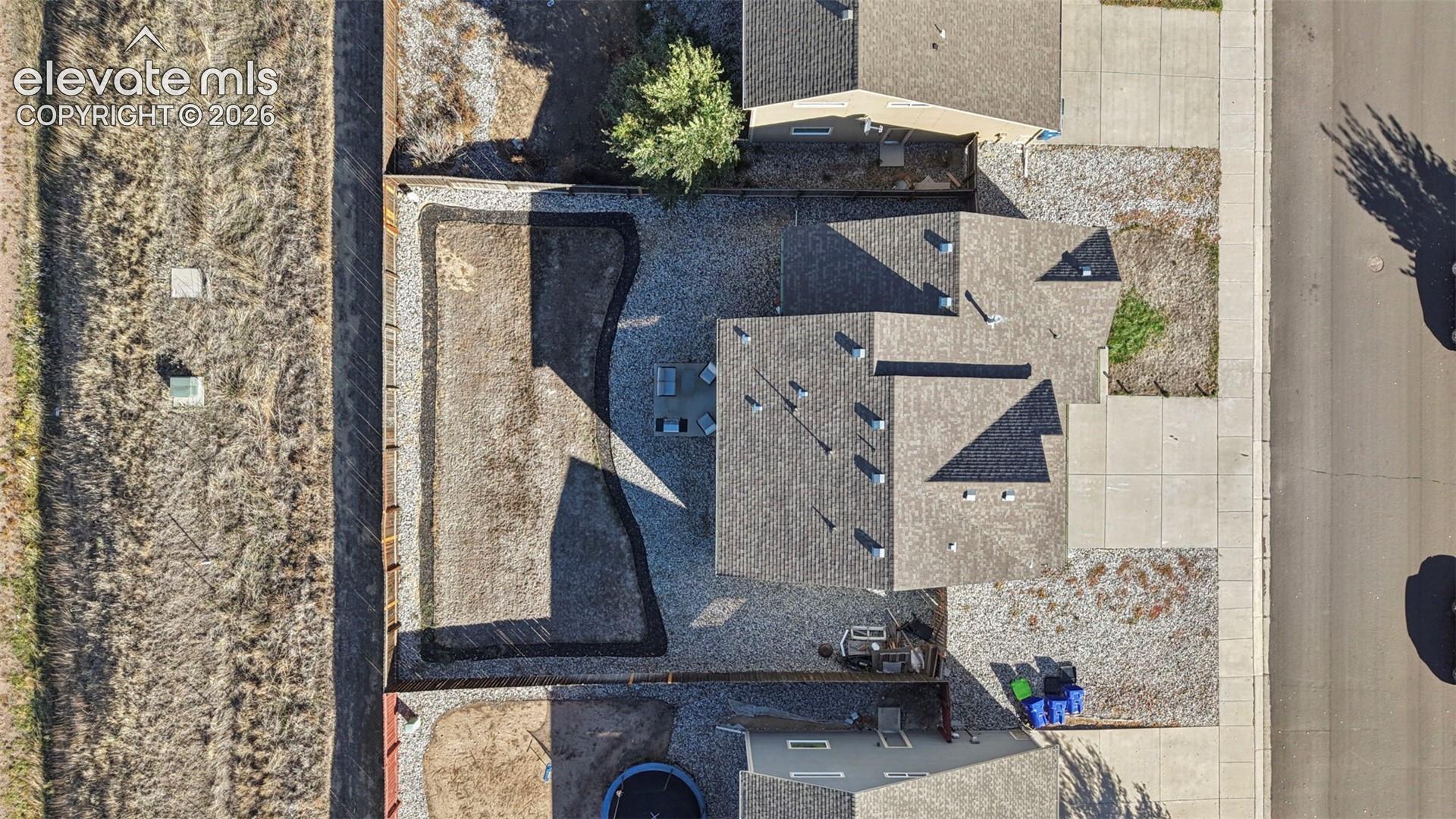 Aerial perspective of residential property featuring a composition-shingle roof, concrete driveway, stone-aggregate landscaping, and a fenced backyard