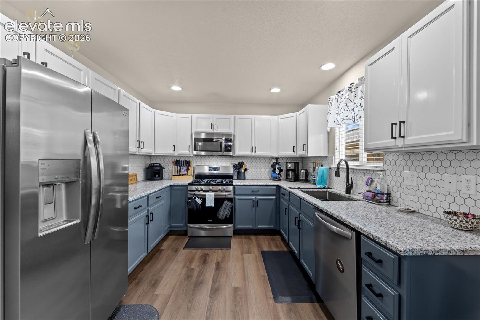 Stainless steel appliances, wood-finish flooring, two-tone cabinetry, hexagon tile backsplash, and recessed lighting