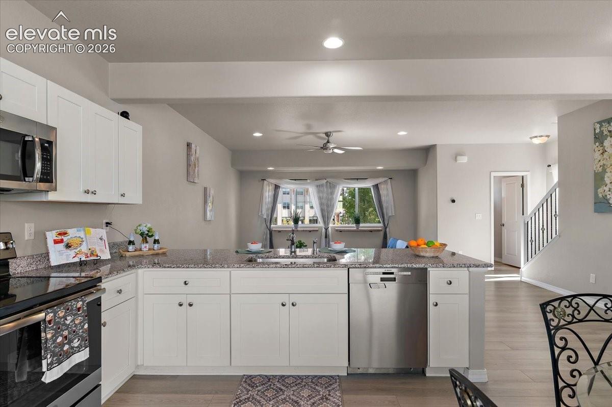 Kitchen featuring white shaker-style cabinetry, stainless steel appliances, speckled stone countertops, and a built-in dishwasher
