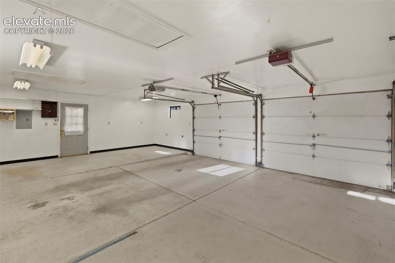 Two-car garage with concrete flooring, two overhead garage doors, and overhead lighting