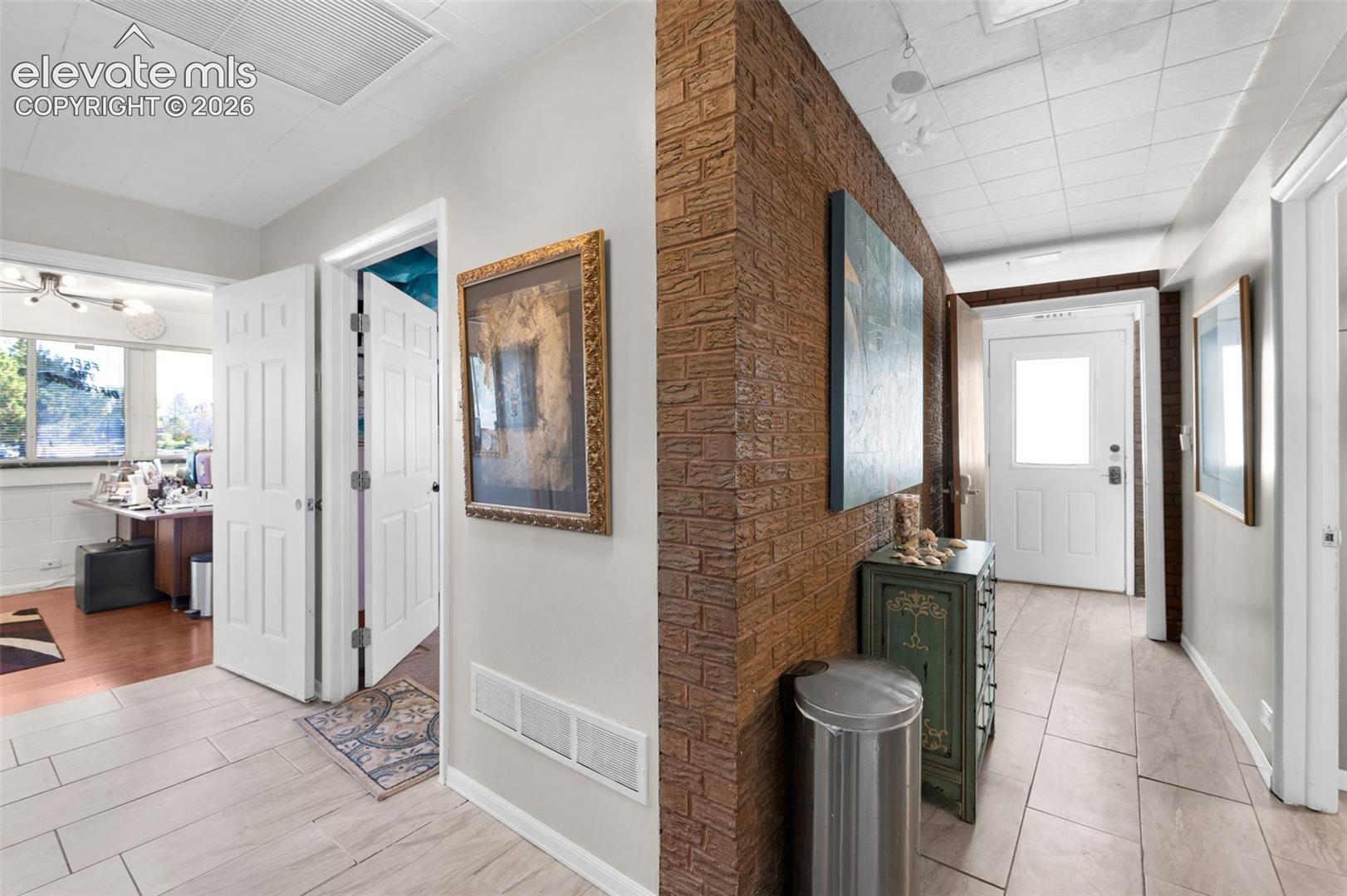 Interior featuring a textured brick accent wall, neutral-toned tile flooring, and solid-core panel doors